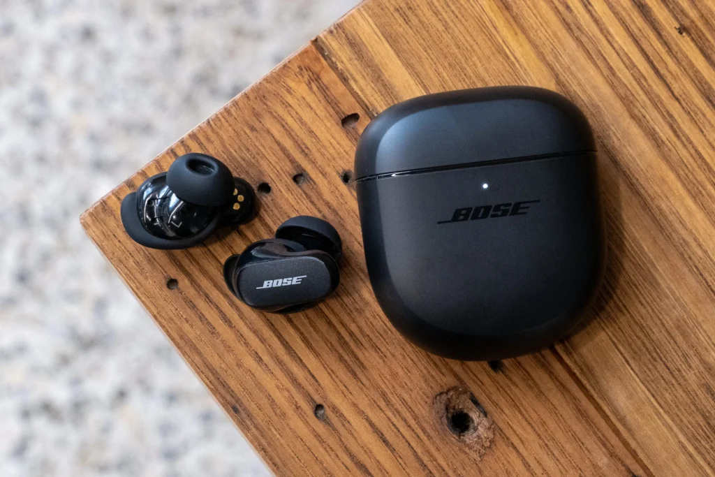 Bose QuietComfort Earbuds II displayed on a wooden table, showcasing their sleek design and charging case